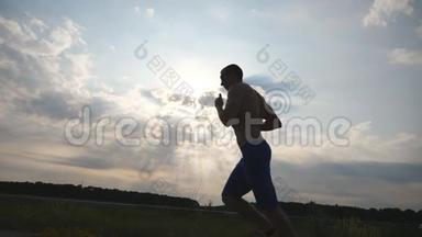 日落时分在乡间小路上慢跑的肌肉男剪影。 男子慢跑训练马拉松跑户外。 运动员
